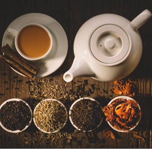 Tea set with teapot, cup, and various tea leaves on a wooden surface