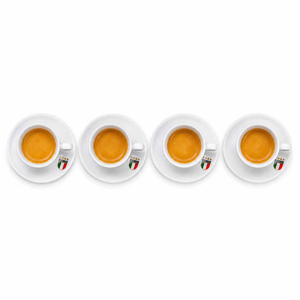 Four white ceramic espresso cups with saucers, each filled with espresso and featuring a small Italian flag emblem on the side, arranged in a row on a white background.