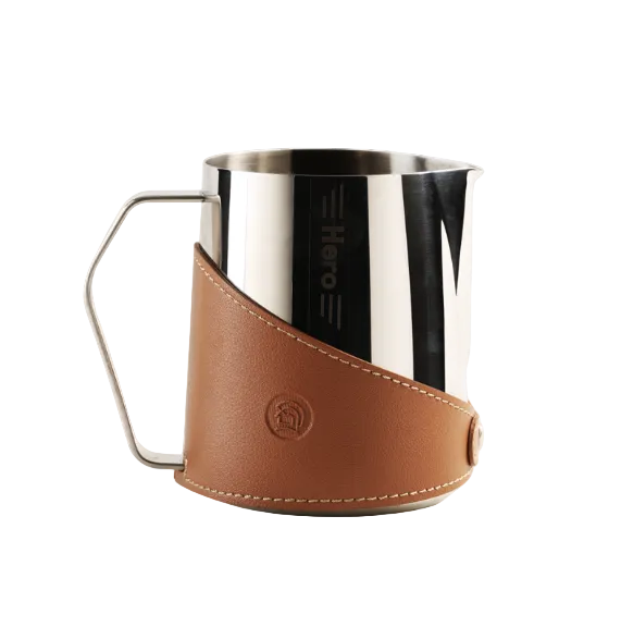 Stainless steel milk frothing pitcher with brown leather sleeve on a white background